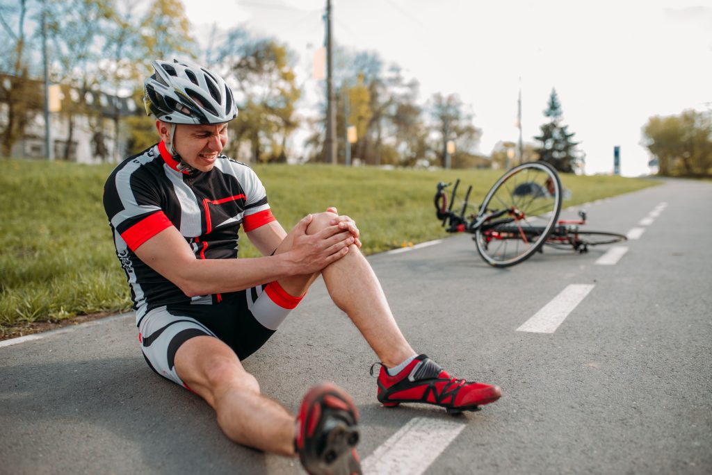 Injured cyclist holding knee on roadside, potential back injury requiring treatment in Malaysia